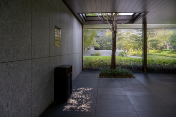 A minimalist lounge or patio in a modern building features a small courtyard visible through horizontal metal slats. The space has a simple aesthetic and a contemporary atmosphere and natural elements