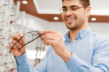 Eyesight And Vision Concept. Happy man choosing new glasses at optics store, selective focus