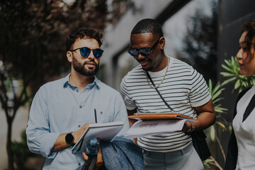 Obraz premium A group of business people in casual attire having a discussion outside. They appear engaged and focused, with documents and notebooks in hand. The setting is casual and professional.