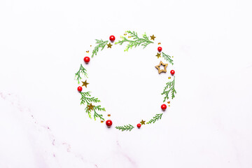 Minimalism style composition with festive Christmas wreath made with fir tree twigs, pine cones and red berries on white background top view, copy space for your text.
