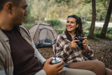 Smiling woman camper holding camera near tent in wooded campsite area