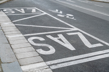 Road markings on asphalt indicate a designated bike lane, and a bus stop area in Europe.