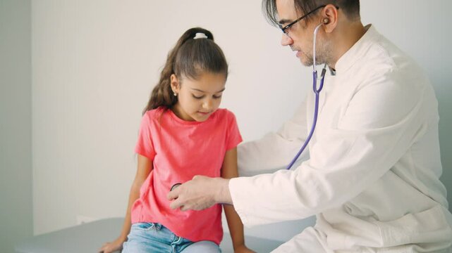 A doctor is thoroughly examining a young girl patient using a stethoscope in a friendly clinical setting that promotes healthcare and wellbeing