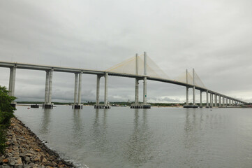 Elegant suspension bridge stretches across serene river under overcast sky.