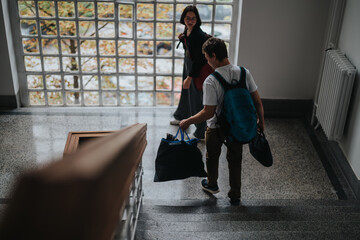 Two students are descending a staircase in a university building, both carrying backpacks. They...