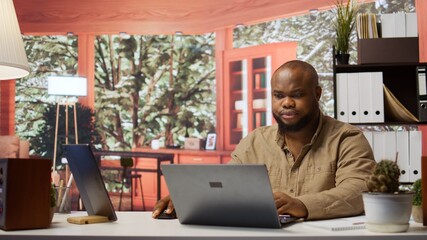 Entrepreneur sitting at his desk working on laptop with wireless technology for remote job...