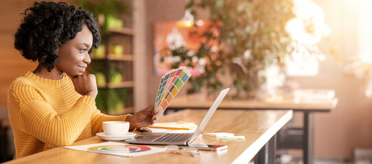 African woman graphic designer working with color sets at cafe, using laptop and drinking coffee,...