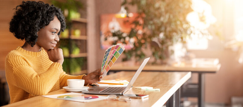 African woman graphic designer working with color sets at cafe, using laptop and drinking coffee, empty space