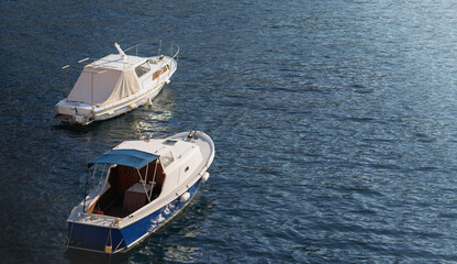 This banner features two small boats floating peacefully on calm, blue waters. The boats are anchored or docked with one of them having a white cover over its cabin, while the other has an open cabin. © Aliaksei Pliutsinski