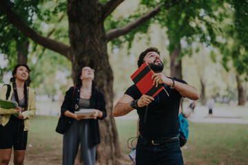 Fototapeta premium Group of diverse students working together on school assignments in a park. The image captures a moment of enthusiasm and teamwork amidst a natural, outdoor environment.