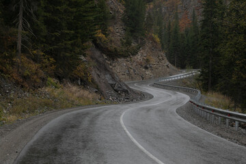 Long curved asphalt road running along the mountain pass. Crash barrier are along the road. Golden...