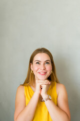 Cheerful young woman is posing in a studio, resting her chin on her hands and looking up with a smile