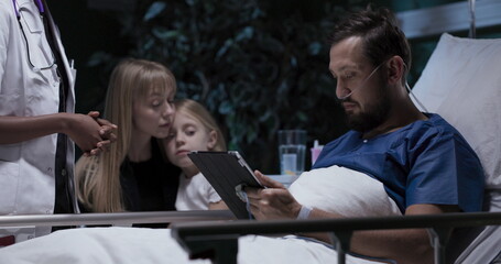 Happy family young man with oxygen tube in nose mother and daughter sit near lovely husband man signs agreement for surgery.