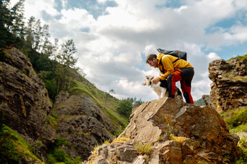 man standing on the rock of a cliff petting his border collie dog while hiking in the mountains. Sports and outdoor activities