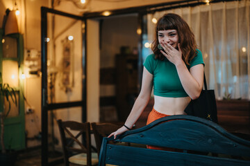 A young woman in a green top smiles warmly in a cozy indoor space. The soft lighting and casual setting create a welcoming and cheerful atmosphere.