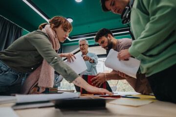 Group of college students working together on a project in a modern classroom with assistance from an elderly professor.