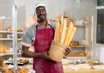 Portrait of confident experienced baker with tasty hot bread and baguettes in hands in kitchen