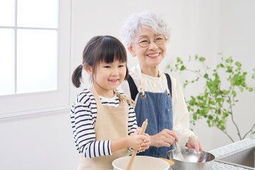 キッチンで料理をする祖母と孫　カメラ目線