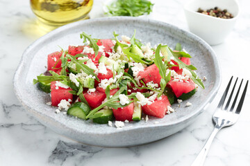Delicious watermelon salad with feta cheese, cucumber and arugula served on white marble table, closeup