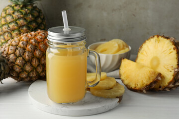 Tasty pineapple juice in mason jar and fresh fruits on white wooden table against grey background, closeup