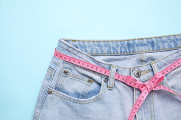 Jeans and measuring tape on light blue background, top view