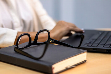 Close-up of Eyeglasses Resting on a Notebook While Typing on Laptop
