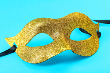 One golden carnival mask on light blue background, closeup