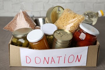 Donation food products in cardboard box on grey table, closeup