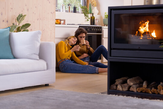 Cozy couple enjoying hot drinks by fireplace in warm, festive home setting
