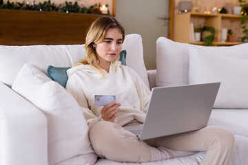Christmas time, Woman shopping online using laptop and credit card, sitting on cozy sofa, at home