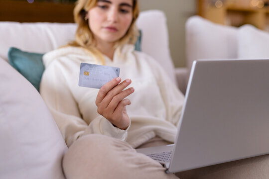 Woman shopping online at home, holding credit card and using laptop