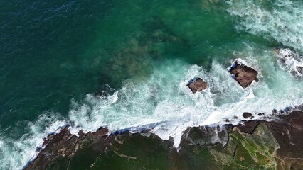 Aerial view drone shot of waves crashing onto rocks near a beach in Australia