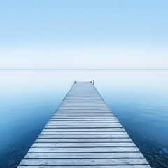 Obraz premium A serene wooden dock extends into calm, blue waters under a clear sky, creating a tranquil atmosphere perfect for relaxation.