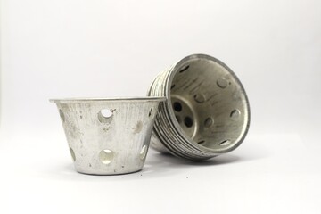 The photo shows a stack of small, round aluminum cups with holes.