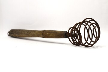 A rusty, vintage wire whisk is lying on a white surface with its wooden handle extending to the left.
