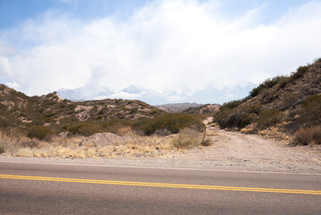 Scene of a roadtrip: driving on an empty road. In the foreground the route, in the background the imposing Andes Mountains in Mendoza, Argentina.