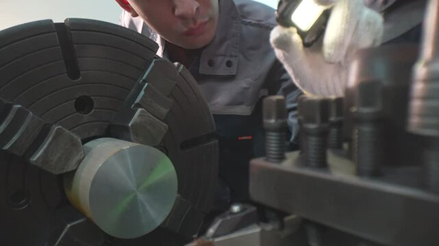Close up of a metal lathe chuck spinning as a technician in gloves adjusts the tool post while machining a steel part in a workshop