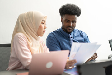 Diverse business team collaborating in modern office, professional muslim woman in hijab and african man discussing project using a tablet, teamwork, multicultural, business communication, leadership