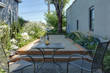 Two chairs beside a table holding a wine bottle and glasses, set amidst a lush garden outside a traditional cottage. Located in Carlton, Oregon.