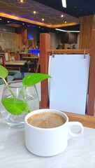 a cup of coffee on the table with a mini vase of green plants and a blank memo. copy space.