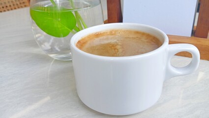 a cup of coffee on the table with a mini vase of green plants and a blank memo. copy space.