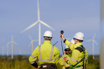 Fototapeta premium A team of engineers in high visibility safety gear stand together at a wind farm, conducting inspections and discussing renewable energy projects. Wind turbines surround them under a clear sky.