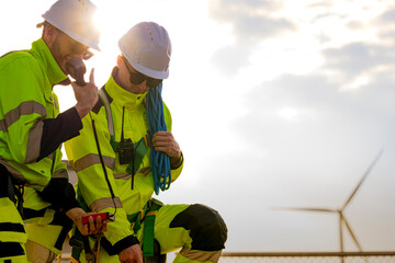 Two engineers wearing high visibility safety jackets and helmets measure wind speed with an...