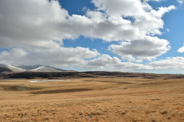 A chain of frozen lakes in the endless steppe at the foot of high snow-capped mountains on an autumn cloudy day.