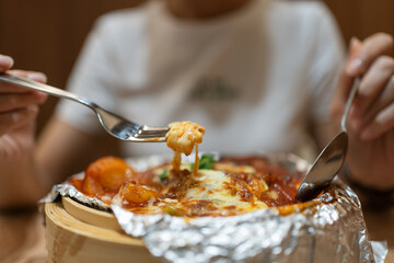 Woman's hand lifts a fork, pulling melted cheese from baked rice.
