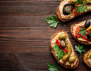 sourdough bread sandwiches with hummus grilled red bell peppers, olives and fresh parsley on a wooden table. copy space