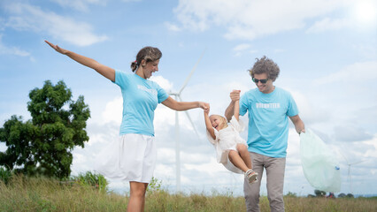A family of three, a man and two women, are playing with a child in a field. The man is holding the child while the woman is holding a bag. The family is wearing blue shirts
