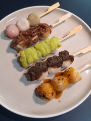Mitarashi, Hanami, Houjicha, Zunda, and Yomogi anko dango on a white plate on navy table. Dango is a traditional sweet in Japan.
