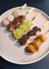 Mitarashi, Hanami, Houjicha, Zunda, and Yomogi anko dango on a white plate on navy table. Dango is a traditional sweet in Japan.