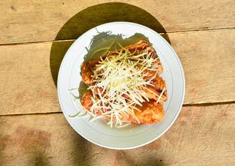Pisang Goreng Keju or Fried Banana Cheese serve with cheddar cheese graters on white plate on the wooden table.